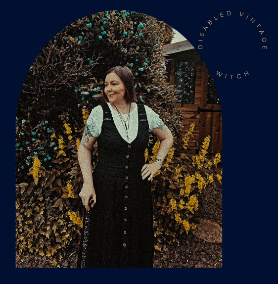 Beverley a white woman is stood in front of yellow flowers. She is standing looking off to the left, dressed in a long black dress and white top and using a walking stick