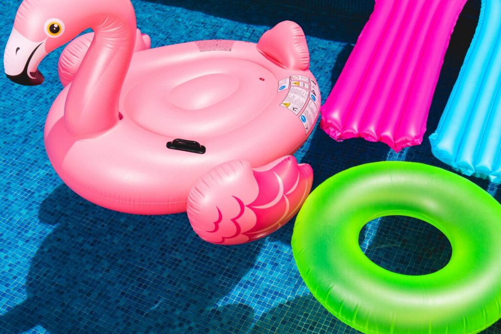 pool floaties one is a flamingo, one a green ring and two loungers one pink and one blue are seen floating in a pool